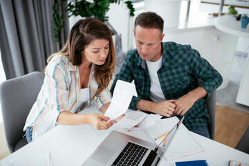 Husband and wife preparing bills to pay. Young couple using laptop.