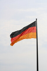 Close up of the national flag of Germany on Reichstag rooftop in summer. Black, red and gold horizontal stripes. Cloudy blue sky in background. No people.