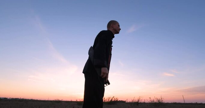 Silhouette of young male kung fu fighter practising alone in the fields during sunset 