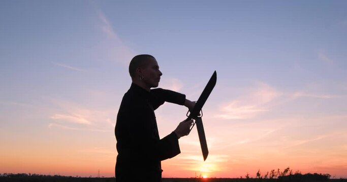Silhouette of young male kung fu fighter practising alone in the fields during sunset 