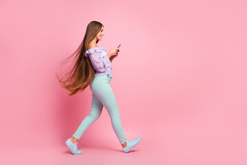 Full length photo of pretty shiny teenager lady dressed casual clothes walking typing modern gadget isolated pastel pink color background