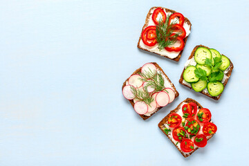 Variety of sandwiches for breakfast - slice of whole grain dark bread, pepper, cream cheese, cucumbers, radishes, cherry tomatoes, garnished with dill, green onions on blue table Top view Flat lay