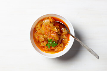 Aubergine appetizer with onion, oil, tomato, garnished with parsley in bowl with spoon on white background