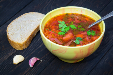 Borscht with parsley in plate on vintage table with garlic and bread. Ukrainian national dish