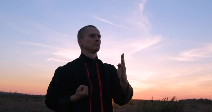 Silhouette of young male kung fu fighter practising alone in the fields during sunset 