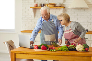 Happy elderly couple cooking healthy vegetarian dinner from online recipe lesson