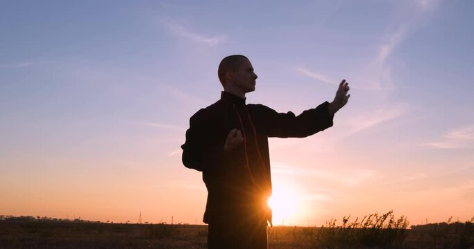 Silhouette of young male kung fu fighter practising alone in the fields during sunset 