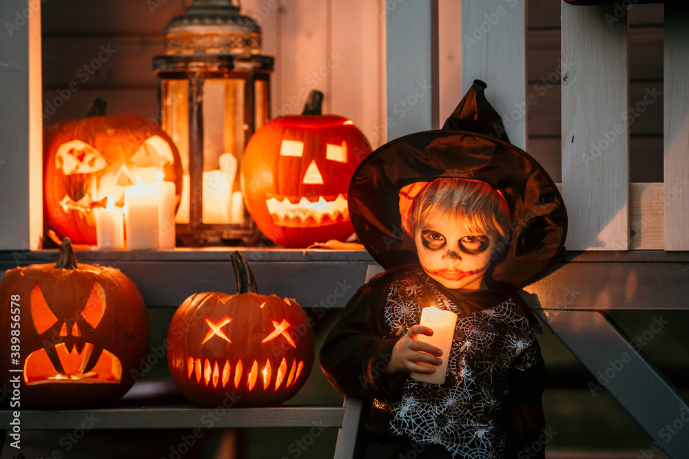 Poster Scary toddler child in halloween costume, playing with carved pumpkins