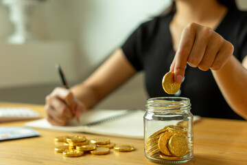 Woman taking note And make income and expenditure accounts by inserting coins in the savings To save money Keep it as retirement money, ideas for saving money for the future