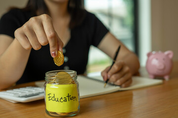 A woman putting money and gold coins in a glass jar And make note of income and expenses for education in the future, ideas for saving money for education
