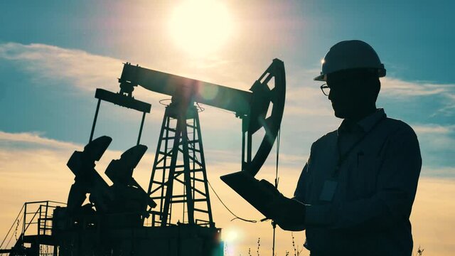 Fossil Fuel, crude oil concept. Power worker is observing an oil extraction site and operating a tablet