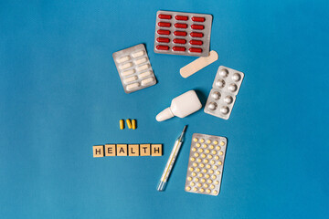 Pills in blisters and a thermometer are photographed from above on a blue background, the concept of health and treatment, space for text.