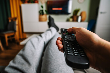 A man is relaxing on the sofa and use the remote control and watch TV in a home with a homely cozy interior