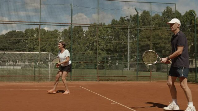 Slow motion video of old couple playing tennis outdoor. They are happy to win so give each other hands. Free time exercise and daily activity. Sport and health theme.