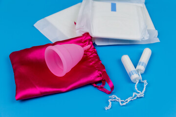 Sanitary pad, tampons and menstrual cup on blue background. Concept of critical days, menstruation, feminine hygiene