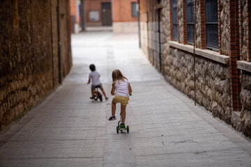 couple of little children running on three-wheeled scooter.