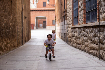 couple of little children running on three-wheeled scooter.