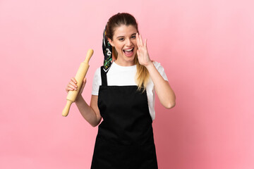 Young blonde woman holding a rolling pin isolated on pink background shouting with mouth wide open