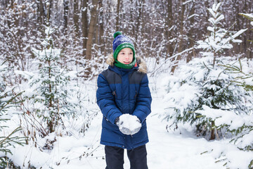 Fototapeta na wymiar Cute young boy plays with snow, have fun, smiles. Teenager in winter park. Active lifestyle, winter activity, outdoor winter games, snowballs.