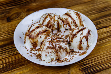 Vanilla ice cream with chocolate topping in white plate on a wooden table