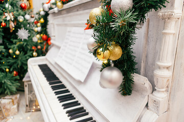 Close-up of silver and gold balls on the fir branch.Blurred old white piano and Christmas tree in the background.New Year and Christmas  concept.Copy space, selective focus with shallow depth of field