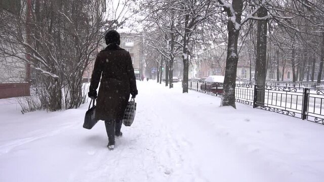 A woman with bags walks through the winter city in the snow, slow motion