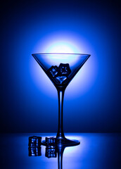 Cocktail glass with ice cubes on blue background and back light.