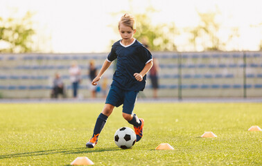 Young boy in blue soccer jersey uniform running after ball on training pitch. Kid improving...