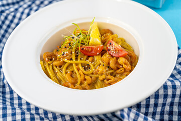 Spaghetti with shrimps, lemon and microgreen. Lunch in a deep white plate, close-up. Pasta with seafood, tomatoes and salad. Food with copy space.