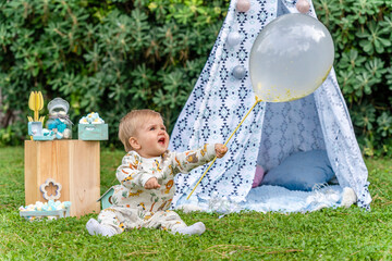 blond baby with blue eyes of a few months playing with a balloon sitting in a teepee tent
