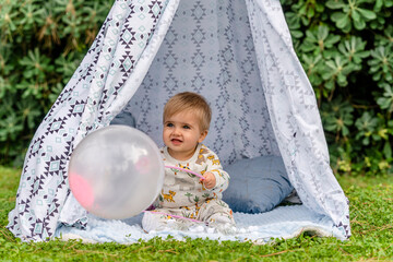 blond baby with blue eyes of a few months playing with a balloon sitting in a teepee tent