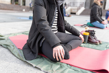 Fototapeta na wymiar Yoga teachers protesting against the blockade and restrictions of Covid-19 in a square in Brescia, Italy. Shot of the hands resting on the knees of the crossed legs. People are meditating.