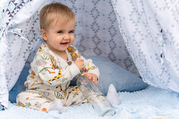 blond baby with blue eyes of a few months sitting inside a teepee tent