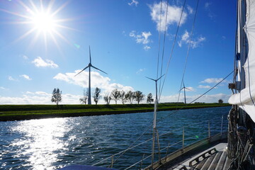 Sunny view from a sailboat on the coast where windmills stand for green energy.