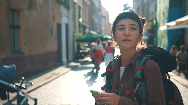 Like to travel alone. Attractive young tourist woman with backpack standing at the street of city, using smartphone to check right address direction way in online map application move forward travel