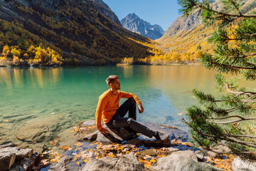 Happy man at the crystal lake in autumnal mountains. Mountain lake and hiker
