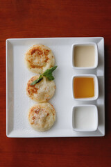 Three cheesecakes and sauce on a white square plate.