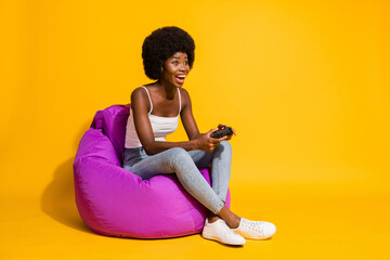Photo of adorable attractive young lady wear casual outfit sitting beanbag enjoying playstation game isolated yellow color background © deagreez