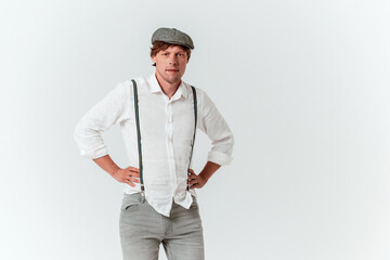 Young man with hands folded on the torso. Male redhead hipster in a cap and white shirt with suspenders. High quality photo.