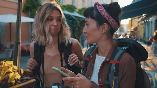We can use the navigator! Two hipster tourist woman standing at the street of old city and using online map on smartphone to find right address hostel or cafe place, traveling together with backpacks
