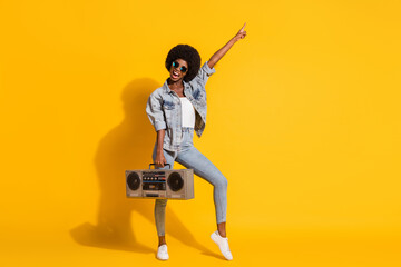 Fototapeta na wymiar Full length photo of adorable lady wear casual denim outfit dancing boombox pointing empty space isolated yellow color background