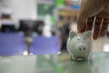 Close up. Hand of a man holding a coin for putting to white piggy bank in the bank office....