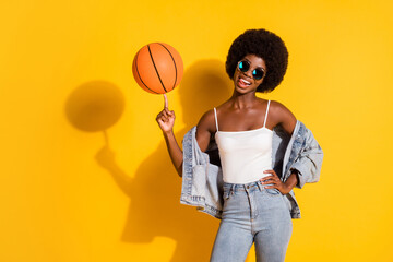 Photo of flirty sportive young lady wear casual denim outfit spinning basketball showing tongue isolated yellow color background