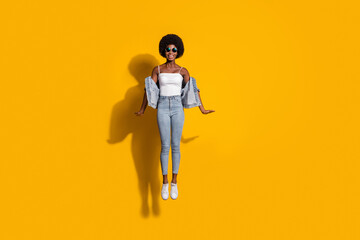 Full body photo of beautiful brown haired woman jump air sport summer wear denim pants singlet isolated on yellow color background