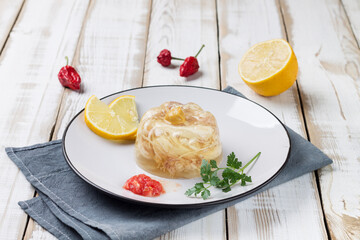 Plate with chicken jelly, decorated with lemon slices, herbs and spices. Natural wooden background