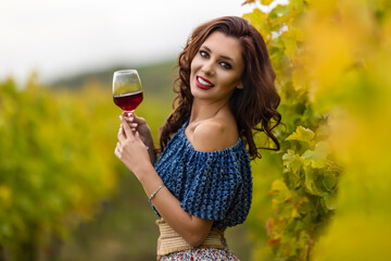 A beautiful woman with a glass of red wine in the vineyard on autumn day.