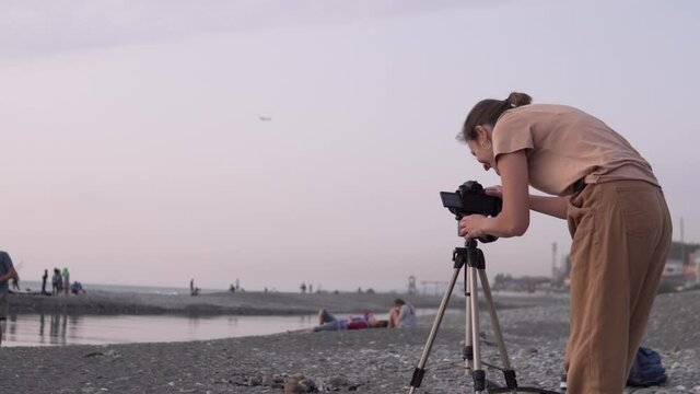 Beautiful female photographer shoots beach at sunset on camera from tripod