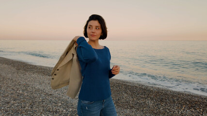 Ragazza con maglia blu e giacca marrone passeggia in riva all'oceano