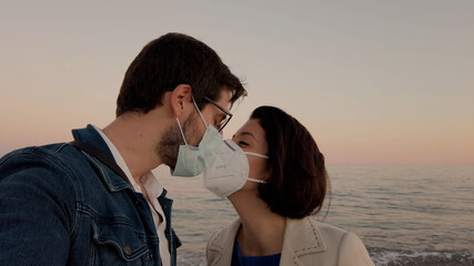 Ragazzo e ragazza si bacia con la mascherina in riva al mare