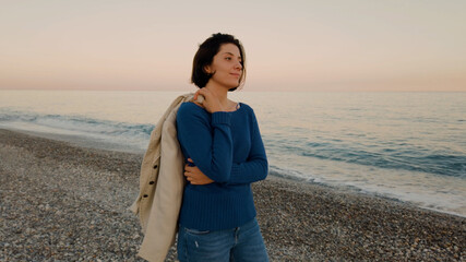 Ragazza con maglia blu e giacca marrone passeggia in riva all'oceano